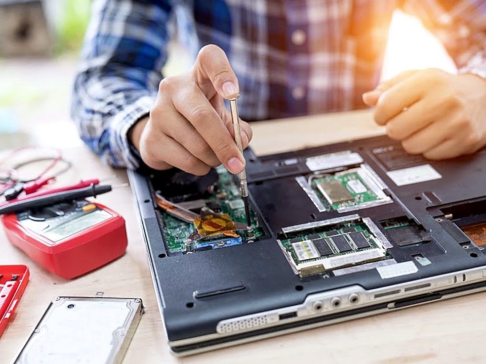 Técnico abrindo um notebook para reparo, com multímetro e ferramentas na bancada